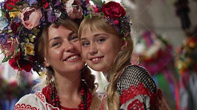Close-up charming girl smiling looking at camera as beautiful woman hugging child. Cute Ukrainian daughter in national
