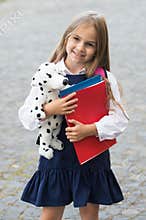 Adding fun to study. Happy child hold toy dog and books outdoors. Back to school supplies. Fashion uniform. Formal dress