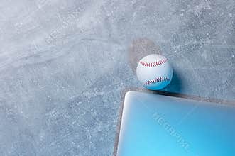 Baseball ball and grey laptop on grey background. Online workout concept