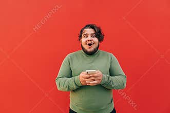 Astonished and excited young hispanic guy with curly hair is looking at the camera with his mouth open, expressing amazement,