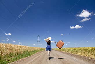 Girl with suitcase at country road.