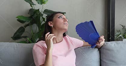 Overheated young indian arabic woman using paper fan.