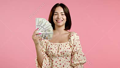 Amazed happy excited woman showing money - U.S. currency dollars banknotes on pink wall. Symbol of success, gain
