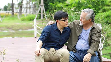 Happy old Asian man pass on his knowledge of life experience to his son while sitting together by the river pier