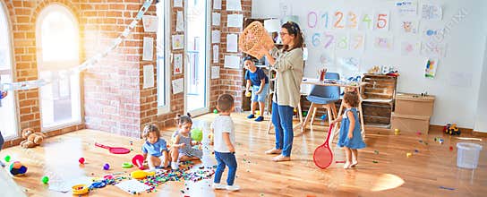 Beautiful teacher and group of toddlers playing around lots of toys at kindergarten