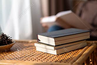 Books on wooden table with blurred of a woman reading book in background