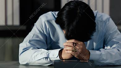 Asian man bowing his head on the Bible and carrying a cross. According to the beliefs of Christianity Is the salvation of Jesus.