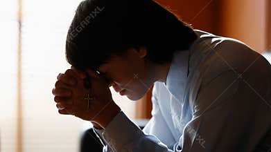 Asian man bowing his head on the Bible and carrying a cross. According to the beliefs of Christianity Is the salvation of Jesus.