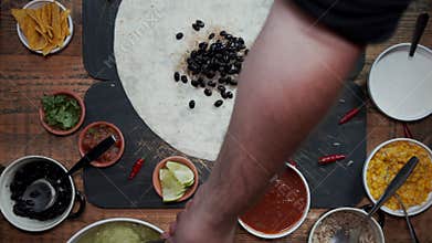 Overhead view of a hand preparing tortilla by adding various fresh healthy ingredients. Top down view of making Mexican