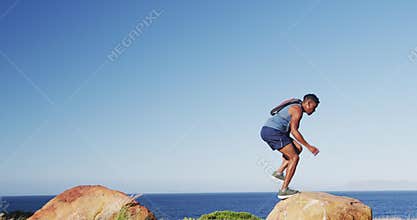 African american man exercising outdoors jumping on rocks in countryside on a mountain