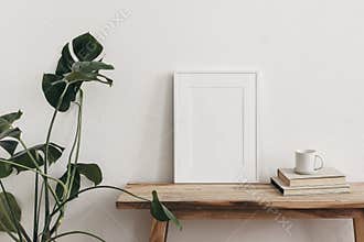 White portrait frame mockups on vintage bench, table. Cup of coffee on pile of books and monstera potted plant. White