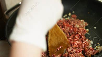 Ground beef and chopped onion and garlic cooking on a frying pan. Mixing with a wooden spatula. Process of making