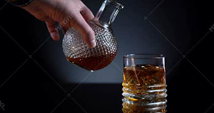 Golden whiskey pouring in the glass from the bottle. With ice cubes. Man takes decanter and pour expensive elite alcohol
