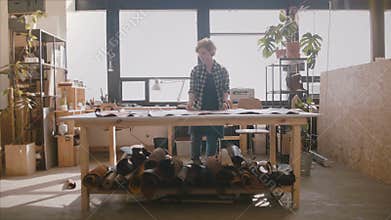 Happy successful female artisan smiling, spreading big pieces of leather on a large table in a manufacturing workshop.