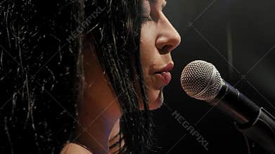 Portrait of a beautiful singer with long hair on a dark stage in the spotlight.