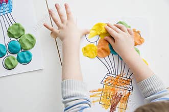 Children hands coloring drawing of house with balloons with colored wax crayons.