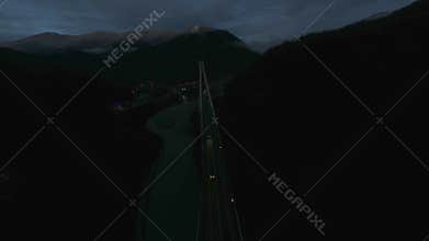 Aerial shot flying over lighting bridge traffic transportation surrounded by mountains at night