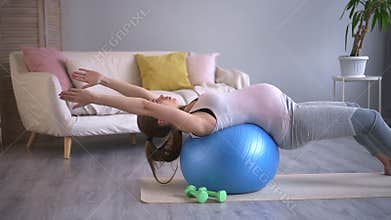 Pregnant woman training with fit ball at home in living room. Lean on back spine, backbend yoga