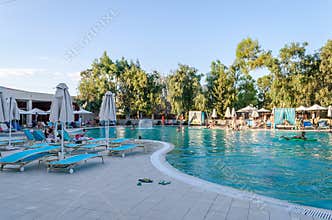 Luxury 5 Star Summer Resort with Pool and Comfortable Sun Beds and Visitors Enjoying the Sun. Stunning Hotel in Greece