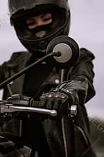 Stylish motorcyclist woman in helmet and leather jacket sitting on black motorcycle. Female driver outdoors on nature
