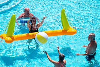 Above view of four senior people playing volleyball in the pool water. Blue color under the sun. Transparent water. Smiles and