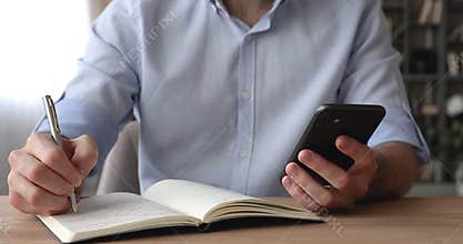 Man sit at desk holding smartphone writing agenda on diary