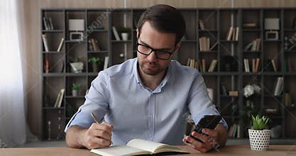 Serious businessman holding cellphone writing notes in agenda