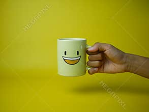 hand holding yellow coffee mug with smile emoticon icon