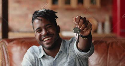 African man sit on sofa showing on camera keys