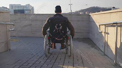 adult man in wheelchair is using handicapped ramp in modern city for moving