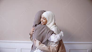 Two muslim girls hugging and smiling in beige studio
