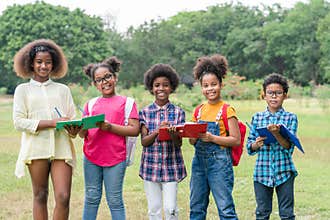 African American childrens holding books and looking at camera while standing in the park