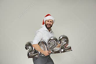 A man in a red velvet Santa hat is holding silver balloons in the shape of 2022