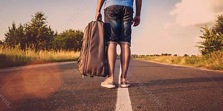 Tourist walks in center of road and carries road bag on summer evening