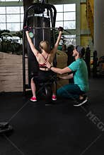 Instructor led training helps a beautiful client to perform exercises in a fitness club, the concept of playing sports