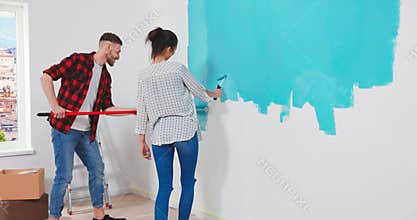 Caucasian happy young just-married couple painting walls in blue color with a wall roller brush