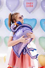 a cute little girl in sunglusses with balloon in the form of a flamingo in hands on many colorful heart balloons