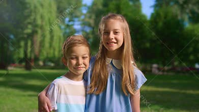 Smiling girl hug little brother looking in camera. Boy unwilling to embrace.