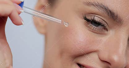 Close-up beautiful young woman applying skincare serum on her face. Skincare concept.