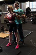 Instructor led training helps a beautiful client to perform exercises in a fitness club, the concept of playing sports