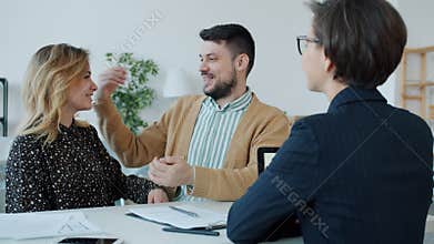 Slow motion of happy young couple buying house getting key from real estate agent hugging