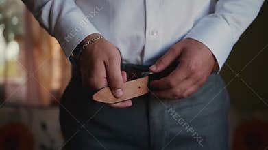 Man in pants and shirt and with silver bracelet unbuckles and tightens belt