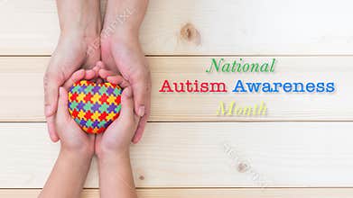 National Autism Awareness month concept with puzzle or jigsaw pattern on heart with autistic child`s hands supported by nursing