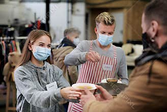 Volunteers serving hot soup for homeless in community charity donation center, coronavirus concept.