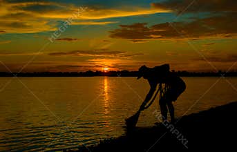 Silhouette of Thai Fisherman catching the fish in twilight  Beautiful Sunset in the sky with sky blue and orange light of the sun