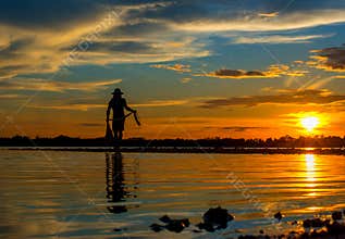 Silhouette of Thai Fisherman catching the fish in twilight  Beautiful Sunset in the sky with sky blue and orange light of the sun
