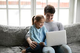 Smiling little girl enjoying watching cartoons on laptop with dad.