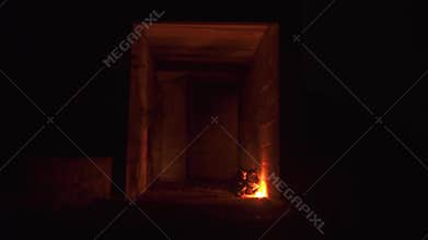 Two mans in a dark sits near the fire in giant abandoned building
