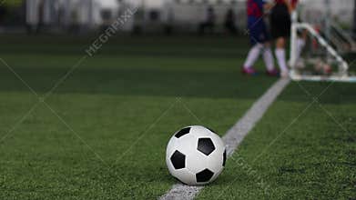 Football on green artificial turf with blurry kid soccer team training.