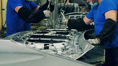 Couple of workers applying structural adhesive on a vehicle part surface. Automobile factory interior.